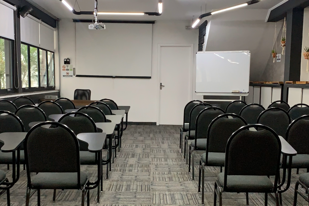 Auditorio com cadeiras universitarias, flipchart e tela de projeção